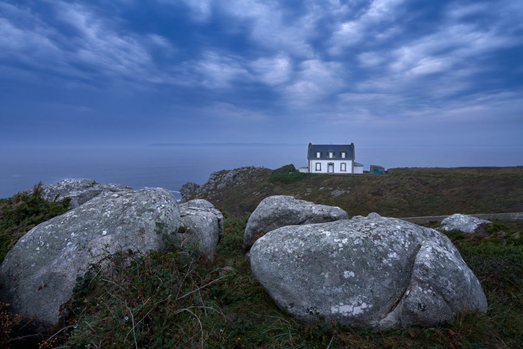 white and blue house on top of gray rock formation under blue sky and white clouds