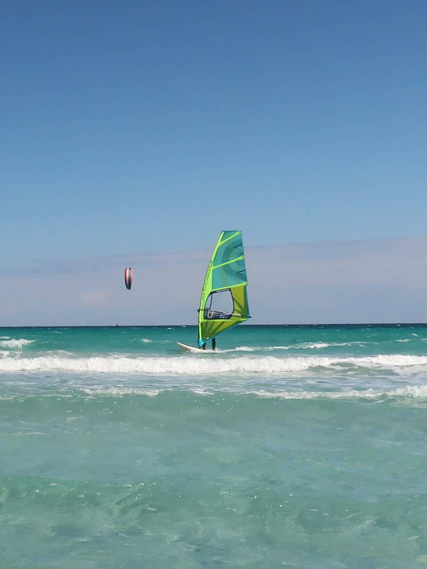 Windsurfer mit blau-grünem Segel auf blauem Meer